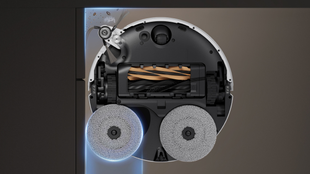 Vista dal basso di un aspirapolvere robot bianco e nero, con due spazzole circolari grigie e una spazzola rotante interna.