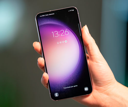 Mano che tiene un telefono con sfondo viola e rosa. L'orario visualizzato sullo schermo � 13:26.