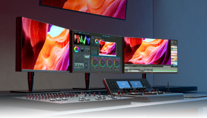 Tre schermi mostrano immagini colorate e software di editing video. Una console con pulsanti e schermi � in primo piano.