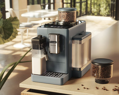 Macchina da caffè grigia con contenitore latte e contenitore chicchi, su tavolo con chicchi sparsi. Sfondo luminoso.