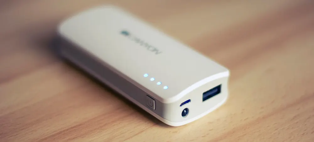 Batteria portatile bianca su superficie di legno. Quattro spie luminose e porte USB visibili.