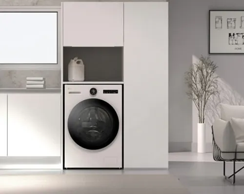 Lavatrice bianca incassata in mobili, con detersivo sopra. Dietro, pianta decorativa e sedia in stanza grigia.