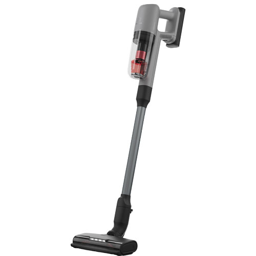 Aspirapolvere verticale grigio con contenitore trasparente che mostra componenti rossi, tubo grigio e spazzola nera.