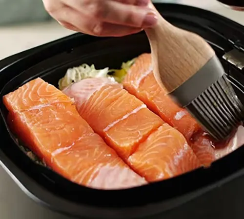 Filetti di salmone in padella nera vengono spennellati con un pennello da cucina in legno.