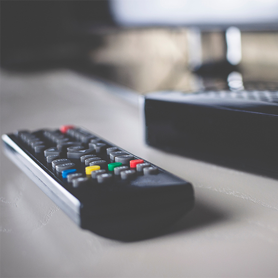 Primo piano di un telecomando nero con pulsanti colorati su un tavolo, con una scatola nera sullo sfondo.