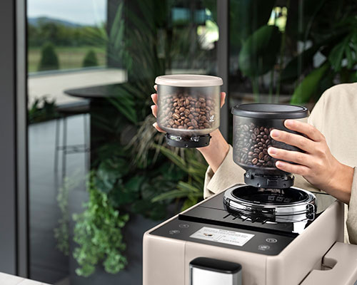 Una persona riempie una macchina da caff� con contenitori trasparenti di chicchi di caff� marroni.