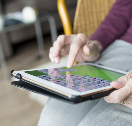 Mani che toccano un tablet con schermo verde e griglia colorata, seduti su una sedia gialla. Sfondo sfocato.