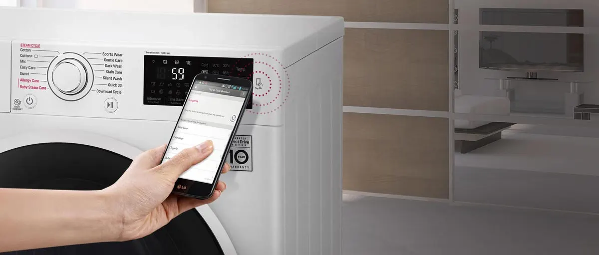 Lavatrice bianca con display digitale che mostra "59". Una mano tiene un telefono vicino al display. Stanza sfocata sullo sfondo.