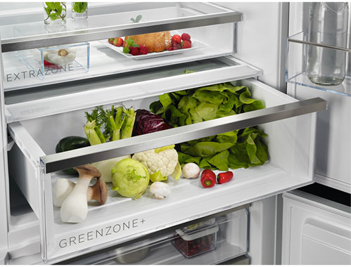 Frigorifero aperto con verdure nel cassetto "Greenzone+", frutta e contenitori visibili.