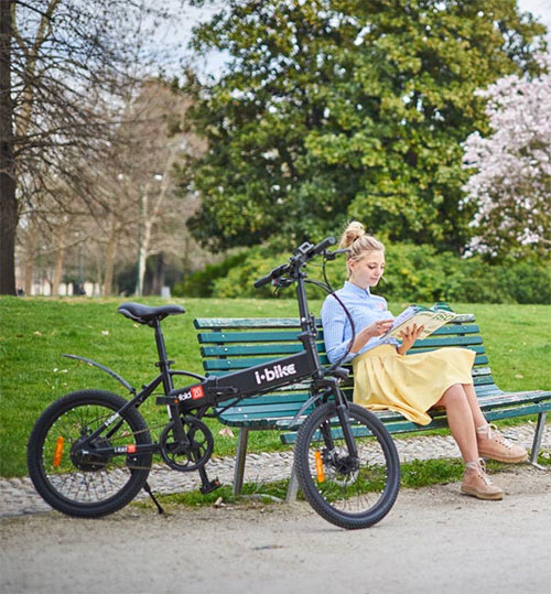 Donna seduta su una panchina verde in un parco, legge un libro. Una bici nera � parcheggiata accanto alla panchina.