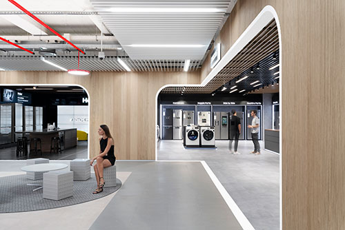 Interno negozio con donna seduta su cubo grigio. In mostra elettrodomestici bianchi e grigi. Illuminazione a soffitto.