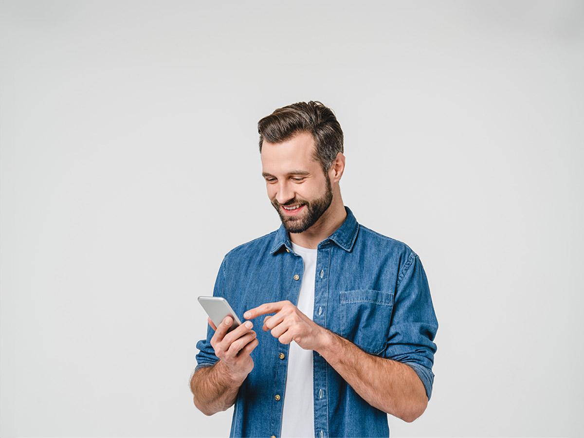 Uomo sorridente con camicia di jeans blu e maglietta bianca che utilizza un telefono su sfondo bianco.