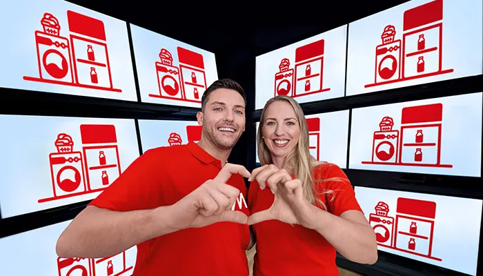 Uomo e donna sorridono, mani a forma di cuore. Sfondo con grafiche rosse di elettrodomestici su schermi bianchi.