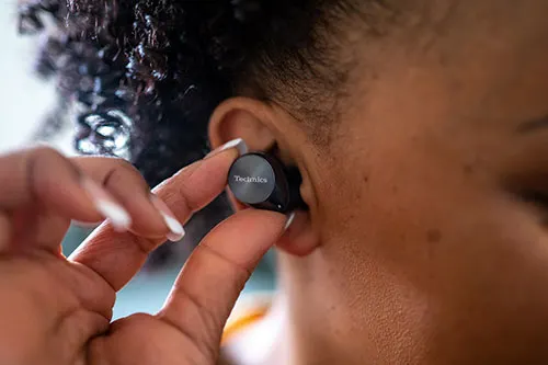 Primo piano su mano che inserisce auricolare nero Technics nell'orecchio di una persona.