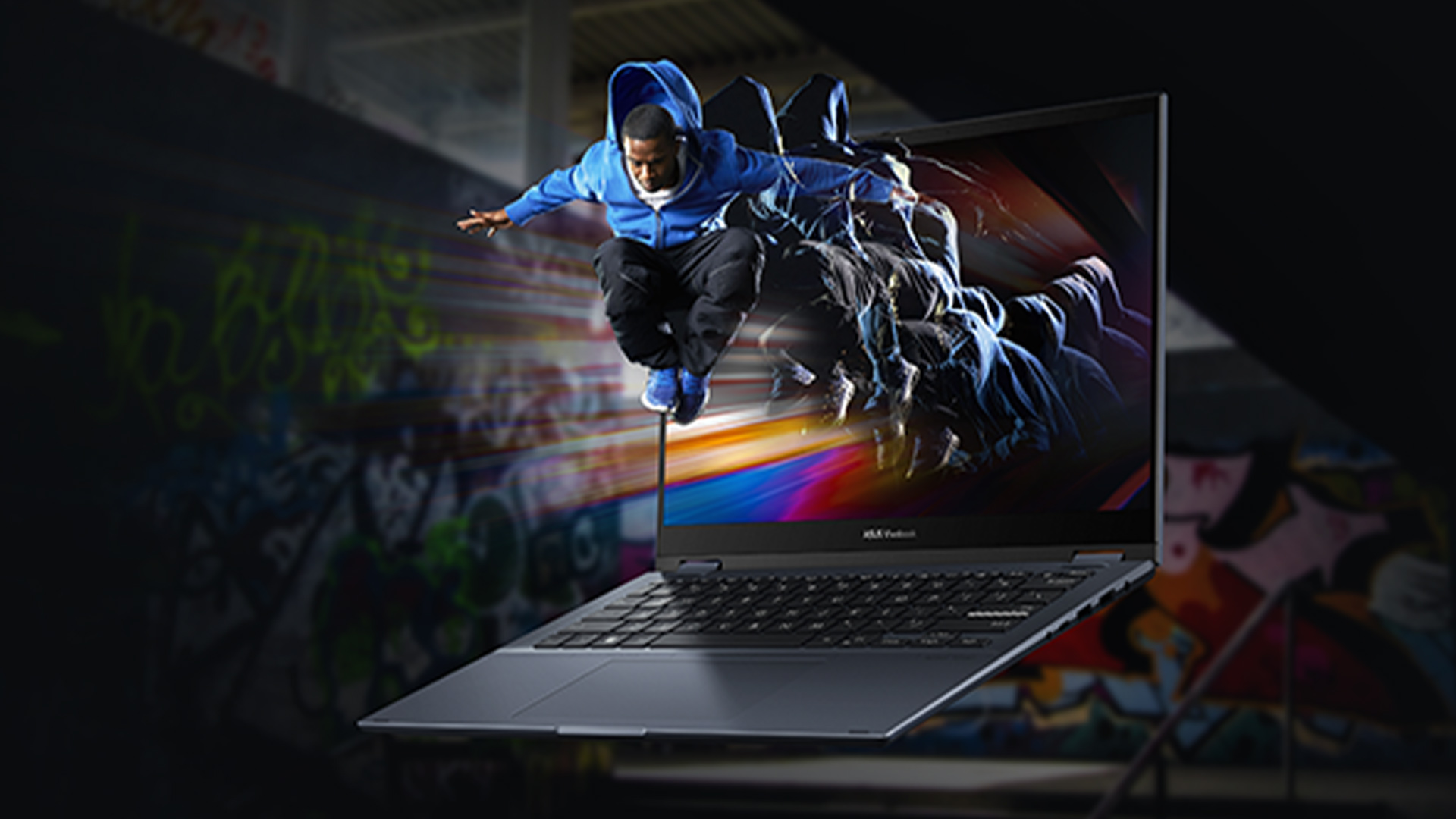 Un uomo in tuta blu salta fuori dallo schermo di un laptop aperto. Lo sfondo è decorato con graffiti colorati.