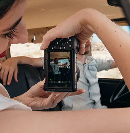 Vista interna di un veicolo: una persona fotografa un'altra persona alla guida. La fotocamera mostra l'immagine.