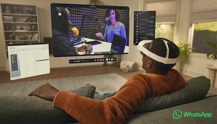 Un uomo con visore VR seduto su un divano guarda schermi virtuali fluttuanti con video e menu.