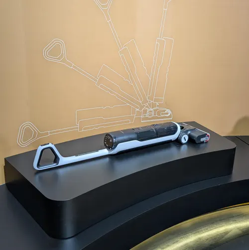 Un oggetto grigio e nero su una superficie nera. Sullo sfondo, uno schizzo bianco su una parete beige.