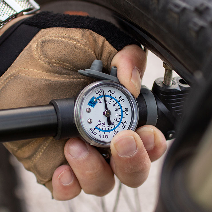 Mano guantata tiene manometro collegato a pneumatico di bicicletta. Il manometro misura circa 120 PSI.