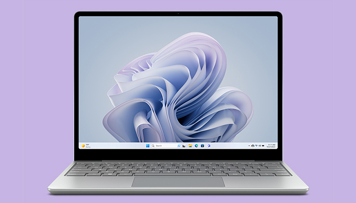 Un laptop aperto mostra lo sfondo di Windows con una forma astratta bianca e blu su uno sfondo azzurro. La tastiera � grigia.