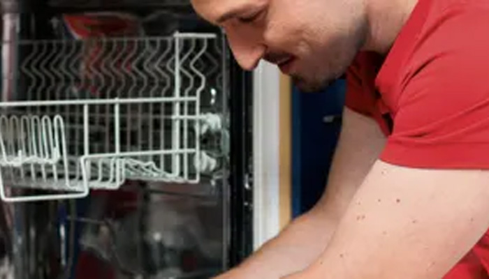 Un uomo in maglietta rossa carica una lavastoviglie con cestelli metallici. Uno sportello è aperto.