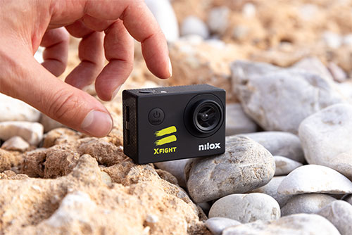 Una action camera nera "Nilox" su sassi grigi e marroni, con una mano che la sfiora.