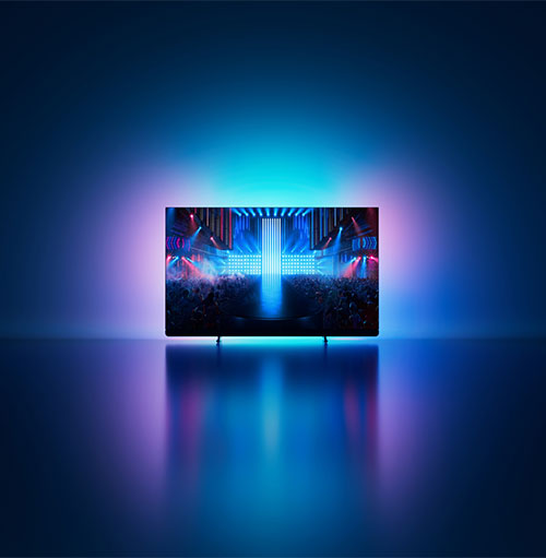 Un televisore mostra un palco illuminato di blu e rosso, con una croce luminosa al centro, su uno sfondo blu.