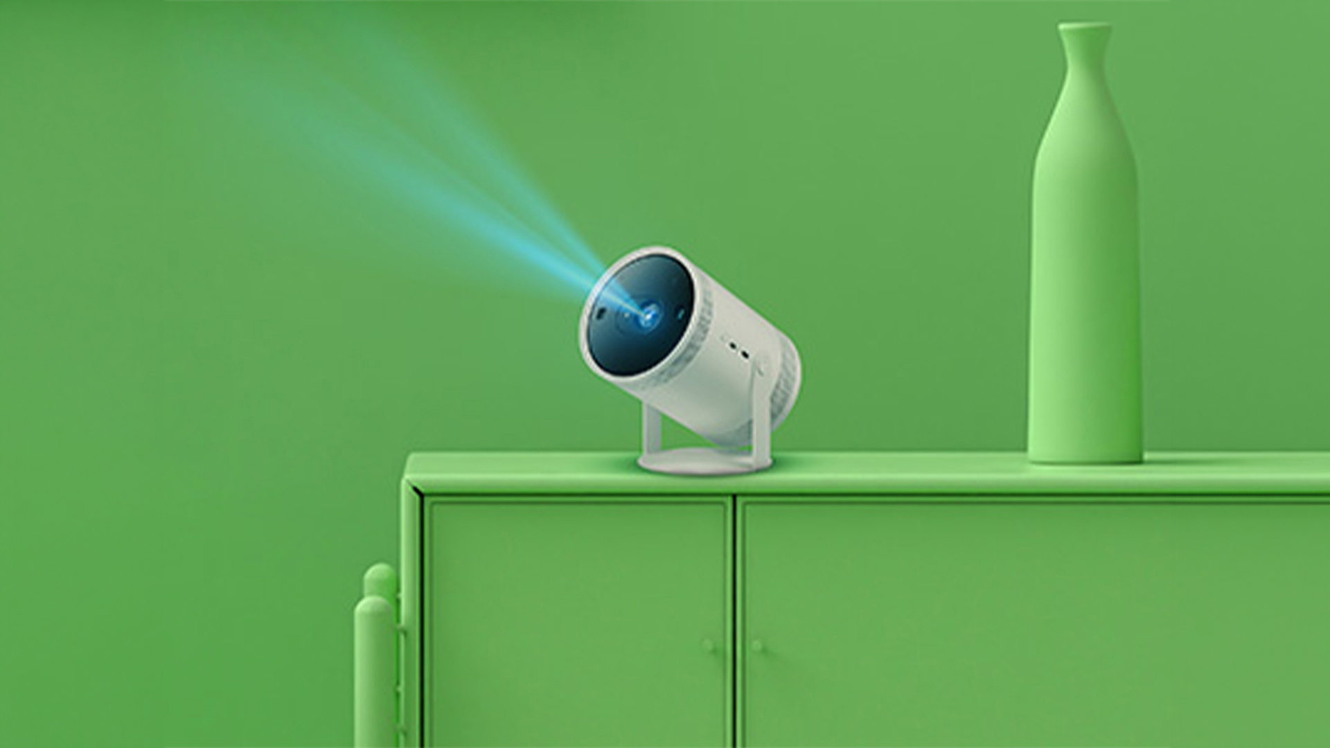 Proiettore bianco acceso su un mobile verde, con un vaso a destra. Il proiettore emette fasci di luce blu.