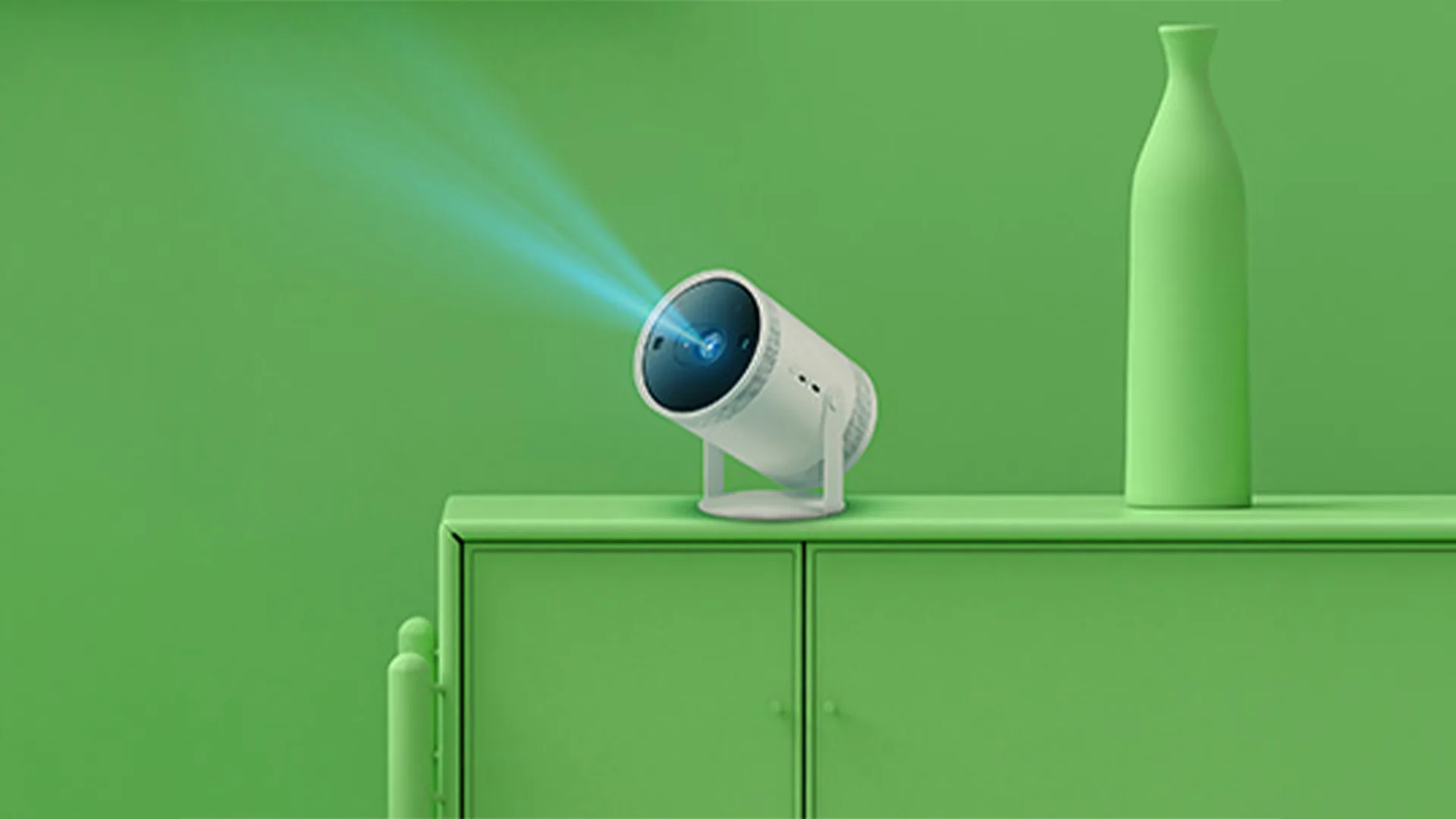 Proiettore bianco acceso su un mobile verde, con un vaso a destra. Il proiettore emette fasci di luce blu.