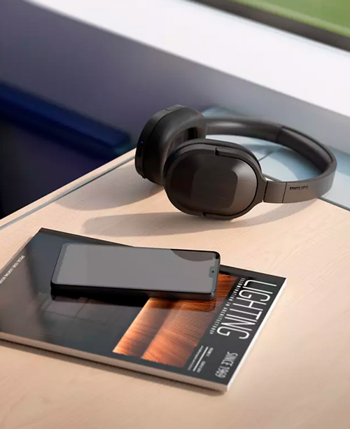 Cuffie nere su rivista con telefono. La rivista mostra la scritta "LIGHTING" in verticale. Lo sfondo � sfocato e include blu e verde.