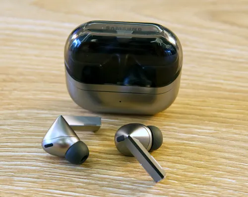 Custodia nera e argento per auricolari wireless, con due auricolari argento e nero su superficie di legno chiara.