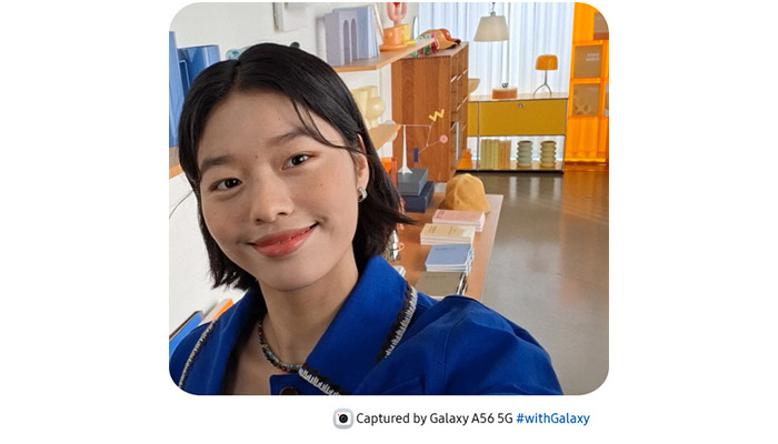 Autoritratto di persona sorridente in giacca blu. Sullo sfondo, scaffali con oggetti decorativi e lampade.