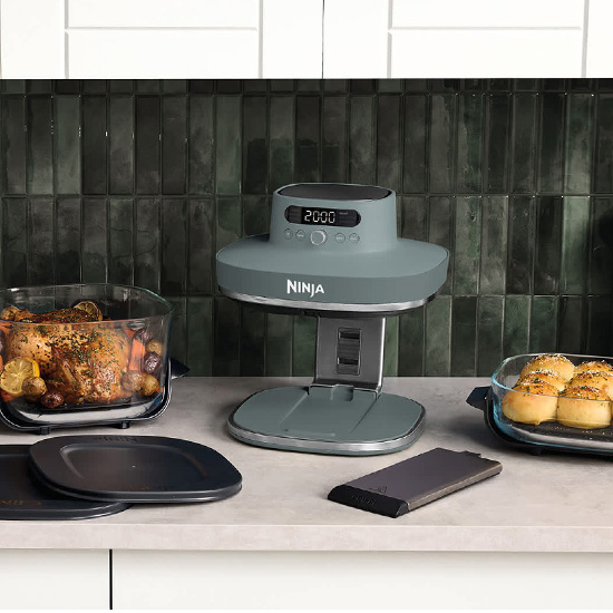 Friggitrice ad aria Ninja verde posizionata sul piano cucina con accanto due contenitori in vetro contenenti pollo arrosto e panini dolci.