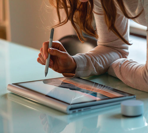 Persona usa una penna su un tablet su un tavolo. Un dispositivo bianco � vicino al tablet.