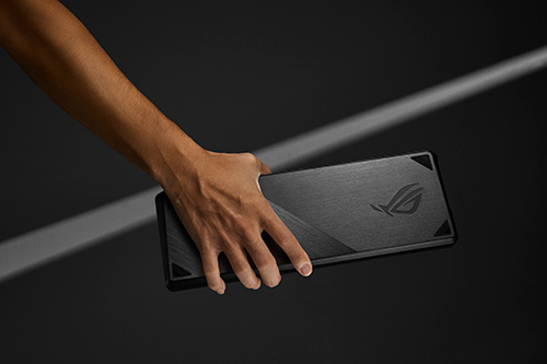 Una mano tiene un dispositivo nero con logo su sfondo nero, illuminato da una luce bianca.