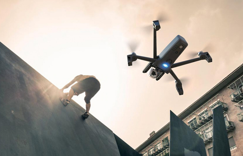 Un uomo si arrampica su un muro. Un drone vola in cielo con un edificio sullo sfondo.