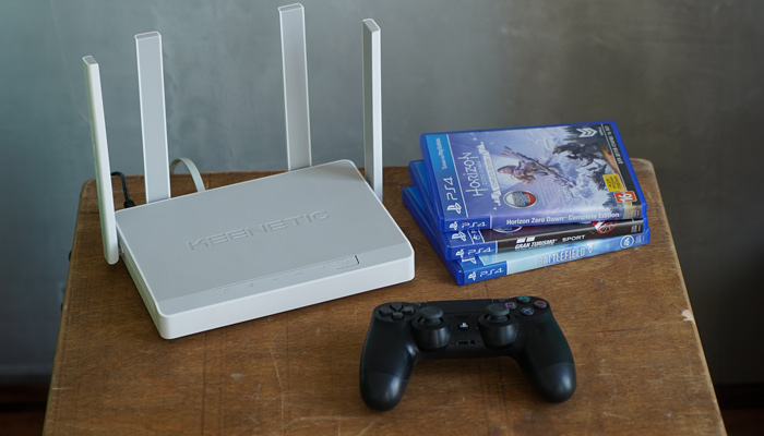 Su un tavolo in legno ci sono un router bianco, dei giochi per PlayStation e un controller nero.