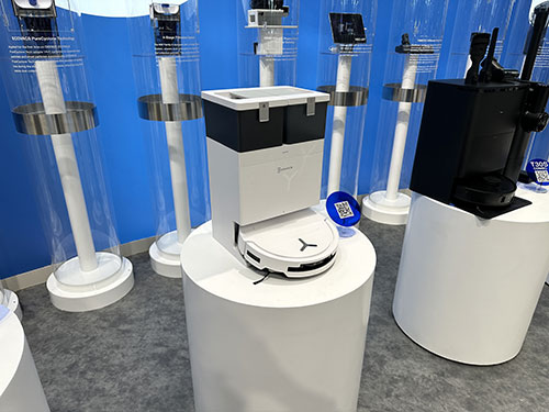 Esposizione di aspirapolvere robot bianchi e neri su piedistalli bianchi, su sfondo blu.