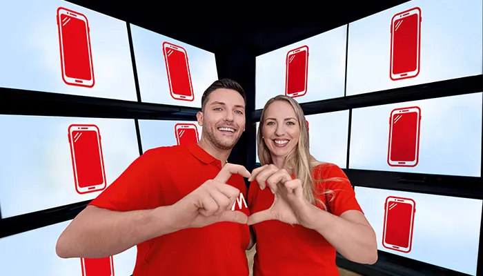 Uomo e donna sorridenti in maglietta rossa formano un cuore con le mani davanti a schermi con icone di smartphone rossi.
