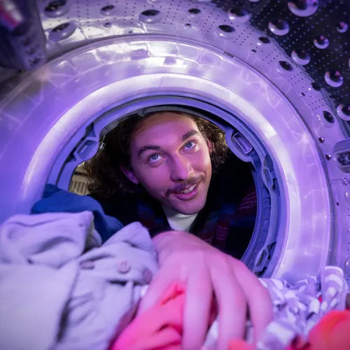 Un venditore in polo rossa mostra lavatrici bianche a un cliente in camicia azzurra, in un negozio illuminato.