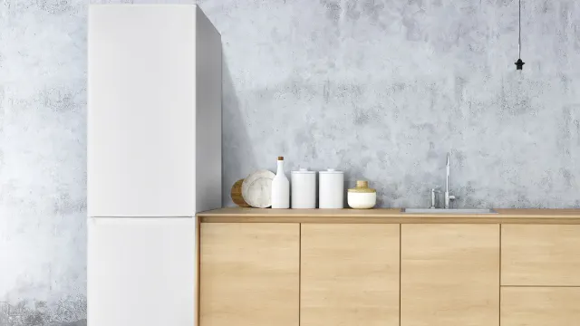 Combinazione frigorifero-congelatore OFK 651 E W di ok., bianca, posizionata libera in una cucina moderna con frontali in legno e parete grigia.