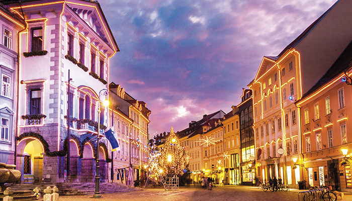 Città illuminata con edifici decorati e un albero di Natale. Biciclette parcheggiate ai lati della strada.