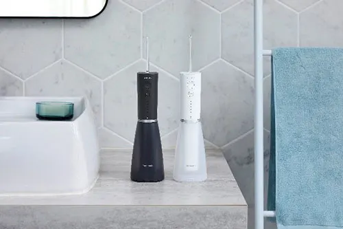 In bagno, due idropulsori nero e bianco su un piano. Lavandino bianco e asciugamano azzurro visibili. Piastrelle esagonali sullo sfondo.