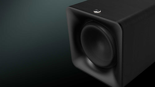 Cassa acustica nera con altoparlante rotondo visibile, su sfondo sfumato scuro.