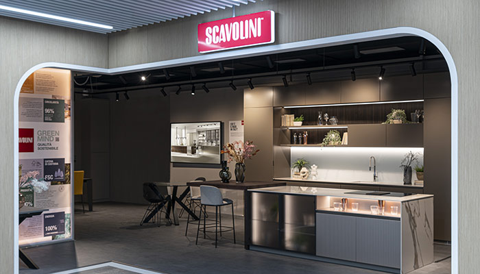 Showroom di cucine Scavolini con isola, tavolo e parete attrezzata. Pannelli informativi a parete e insegna luminosa.