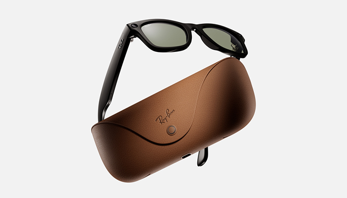 Occhiali da sole neri appoggiati su una custodia marrone con il logo Ray-Ban su sfondo bianco.