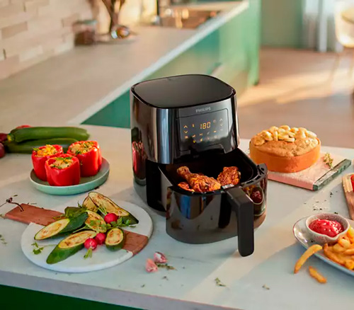 Friggitrice ad aria aperta su un tavolo con verdure, patatine fritte, ketchup, pane e pollo fritto.