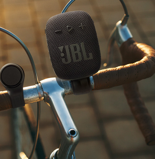 Altoparlante JBL nero montato sul manubrio di una bicicletta argento con impugnature marroni. Cavi visibili.