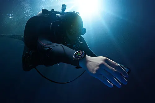 Un subacqueo in tuta nera con orologio in acque profonde illuminate dalla luce solare.
