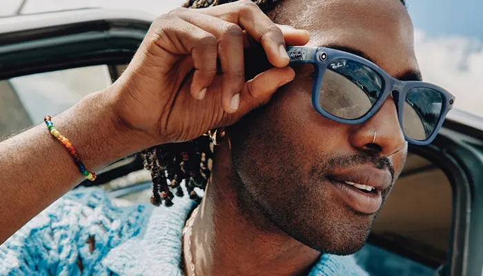 Uomo con occhiali da sole blu, seduto in auto. Un braccialetto arcobaleno è visibile sul braccio sinistro.